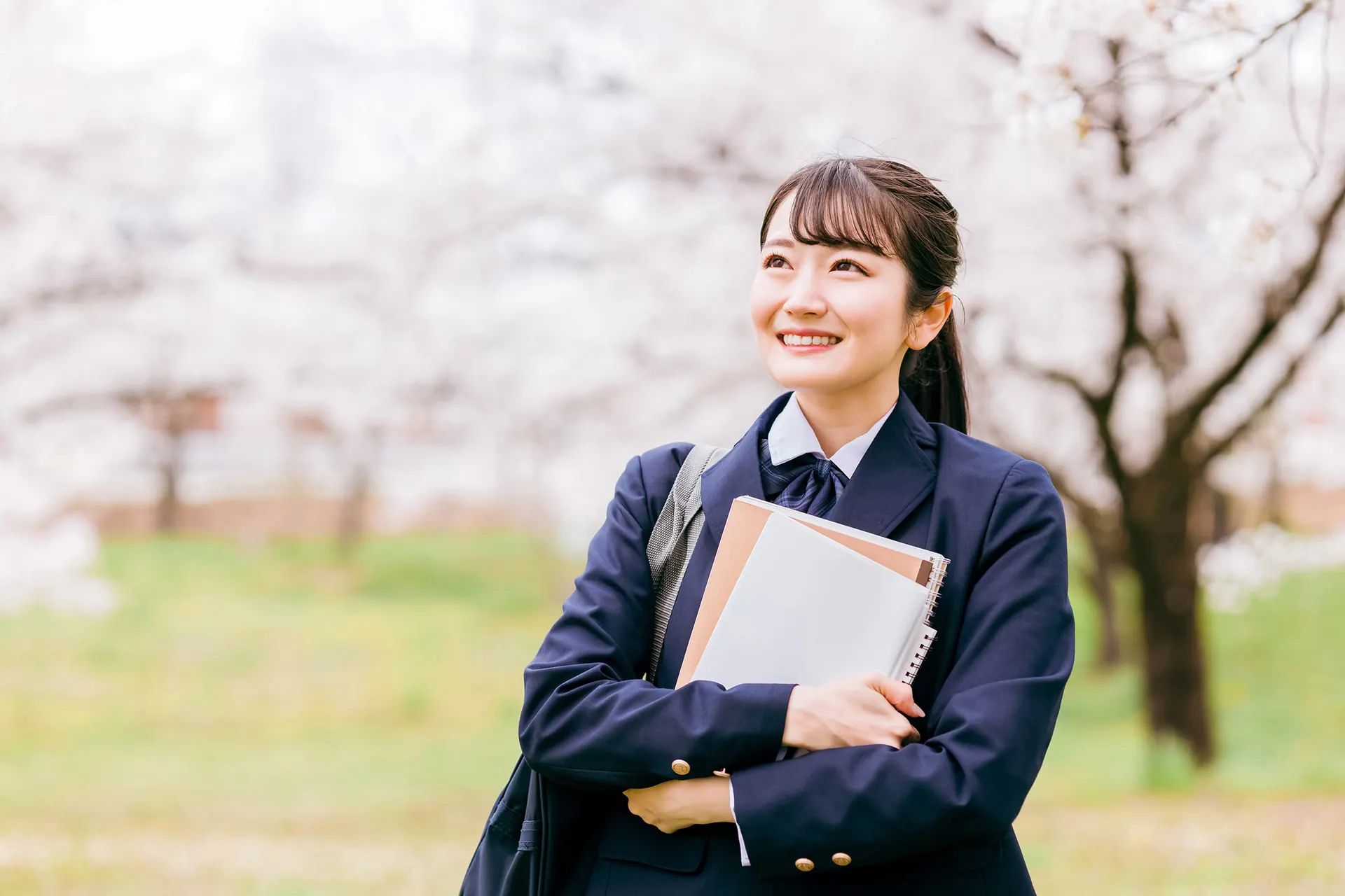 桜の下で笑顔を見せる制服姿の生徒